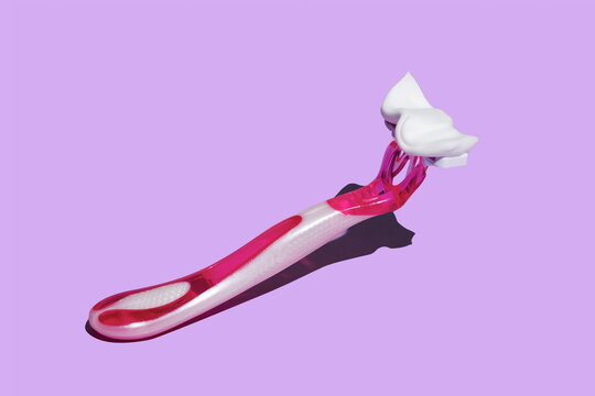 Pink razor with shaving foam on pastel violet background