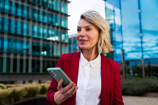 Businesswoman in red blazer using phone in urban business centre
