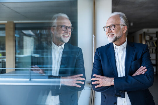 Businessman in suit smiling by window with reflection in modern office