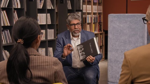 Middle-aged biracial male author in casual suit talking about his new book while giving presentation in library