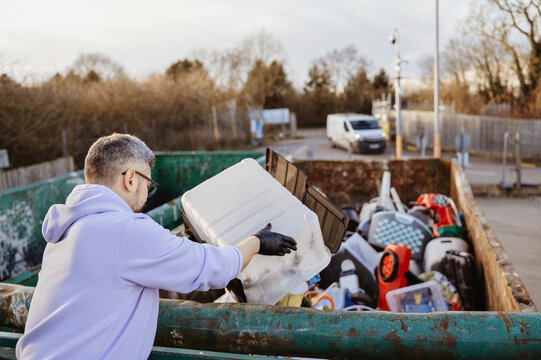 Back view of man recycling large plastic container.