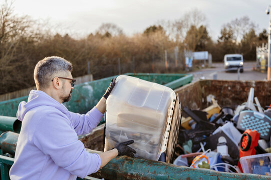 Man disposing of large plastic box into recycling container outdoors.