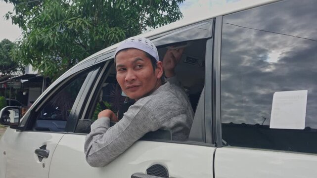 Asian Muslim man in skullcap looking out of car window during Mudik homecoming travel