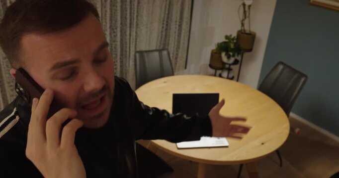 Indoor scene of a man calling IT support while pointing at a malfunctioning laptop on the table. Concept of technical problems, customer service, remote assistance and troubleshooting.