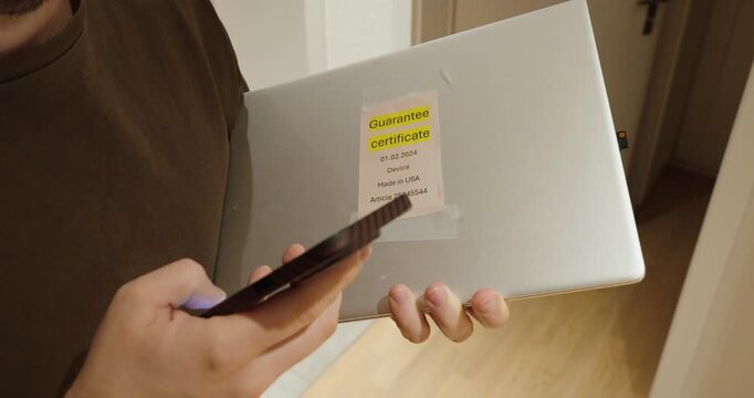 a person holding a laptop with guarantee certificate while using a smartphone to request warranty service. Concept of consumer rights, repair claim, product return and customer support process.
