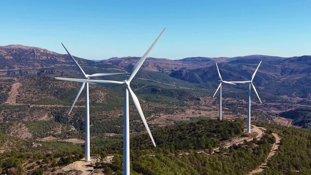 Aerial footage of modern wind turbines spinning along a mountainous ridge, generating renewable electricity with large rotor blades in a remote highland landscape
