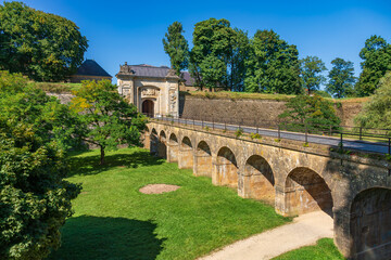 Fototapeta premium Fort Longwy, part of the UNESCO Fortifications of Vauban, with stone bridge, historic gate and ramparts above a green moat in summer, France