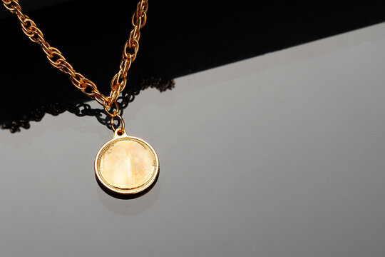 Gold chain necklace with round pendant placed on a dark surface in a studio setting