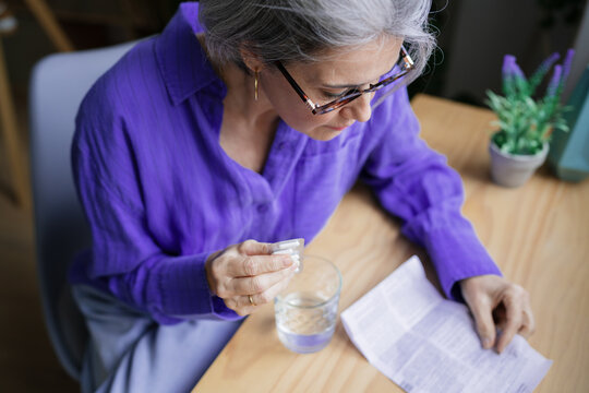 Woman reading instructions and taking medication at table indoors
