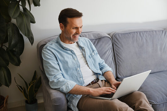Man using laptop while sitting on sofa in cozy home office