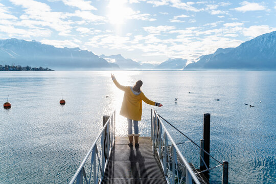 Woman standing on jetty with arms outstretched near sea under cloudy sky