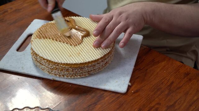 Spreading wafer cakes with condensed milk. Simple cake. Sweet food on table. Hands spread cream with knife. Cook at home