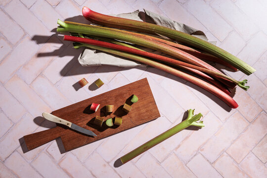 Fresh rhubarb sliced on cutting board with knife on tile background