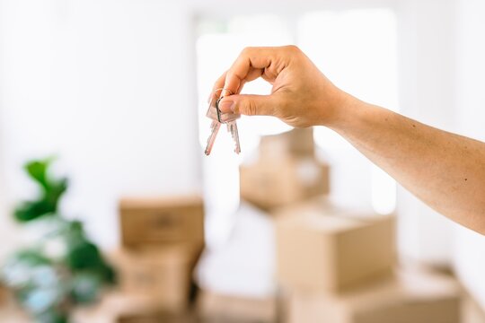 Hand holding keys with moving boxes indoors in new apartment