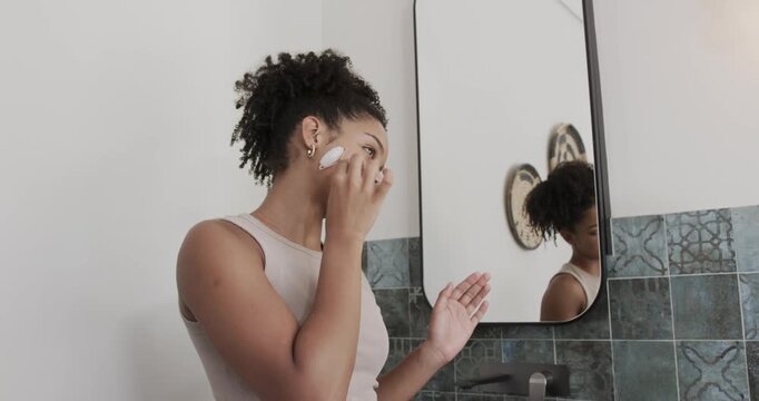 African American woman placing facial device on cheek switching to lip wand at sink checking mirror