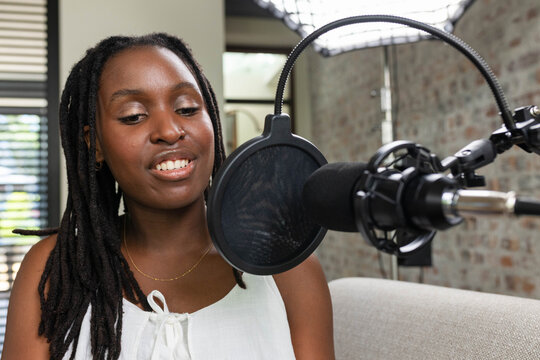 African woman recording into condenser mic in home studio wearing white sleeveless top, copy space