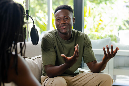 Diverse pair recording interview in studio with mic pop filter, African man in olive tee gesturing