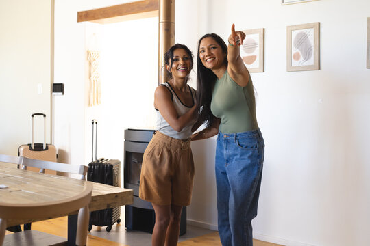 Diverse female friends standing in bright living room pointing at wood-burning stove and suitcases