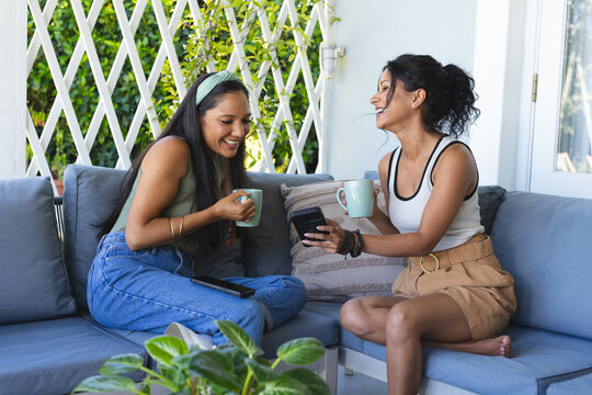 Ceramic mugs sitting on gray sectional sofa in covered patio sunroom, smartphone nearby