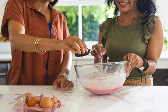 Clear glass mixing bowl with pink batter is being whisked while extract is pouring near window