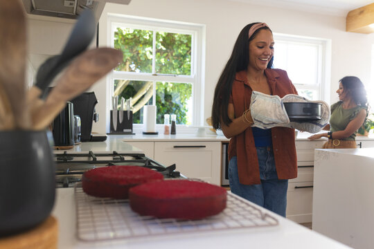 Two round red cakes are cooling on wire rack on kitchen countertop near gas cooktop