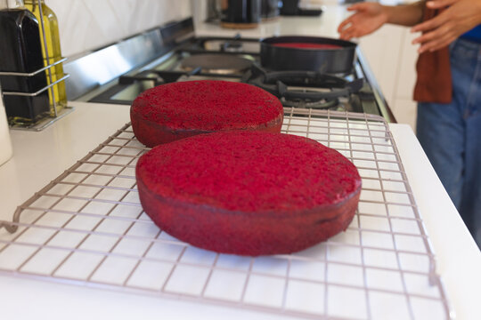 Two red cake layers are cooling on metal wire rack on white countertop in home kitchen
