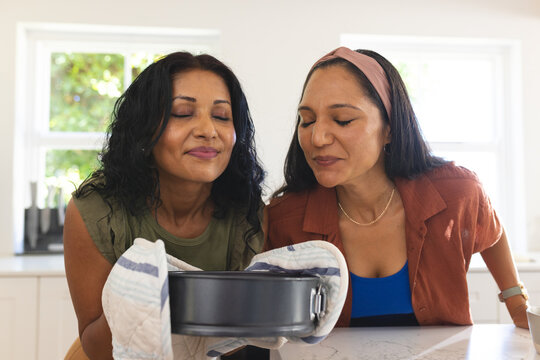 Diverse female friends leaning over springform pan on folded kitchen towel in modern home kitchen