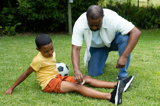 Black-and-white soccer ball resting on grass while scraped knee is being cleaned near shrubs