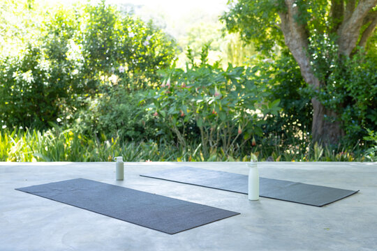 Two gray yoga mats are lying on patio with white water bottles near tops, overlooking garden