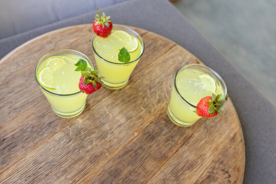 Three glasses sitting on wooden table holding citrus drinks with strawberry, lime, mint, copy space
