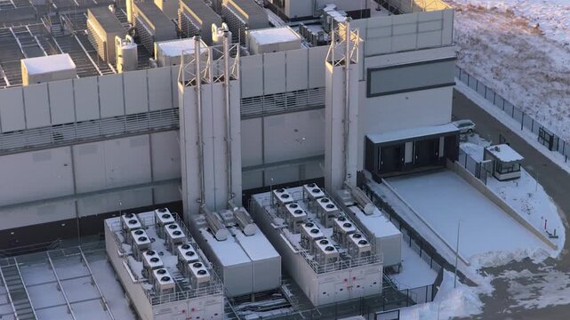 Industrial data center building with its cooling and ventilation systems covered in snow. An aerial orbit reveals the infrastructure.