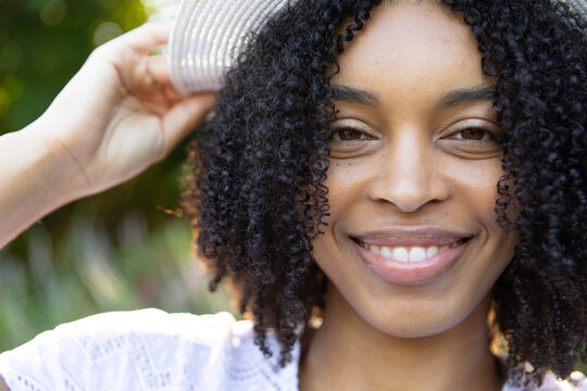 African American woman smiling, holding sun hat with left hand, wearing white lace top in garden