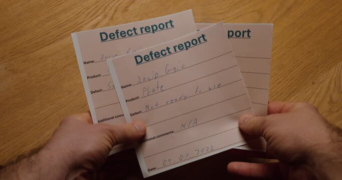 hands holding several defect report forms on a wooden desk. Concept of quality control documentation, nonconformity management, compliance procedures and industrial reporting process.
