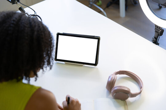 Tablet is displaying blank white screen on stand while pink headphones are resting on white desk