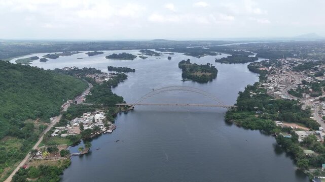 Wide drone panorama of the Adomi Bridge over the Volta River in Akosombo, Ghana. High-angle view of West African infrastructure, lush tropical river banks, and scenic nature landscape