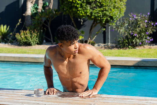 African American man in swim trunks exiting pool onto backyard deck near glass with citrus wedge