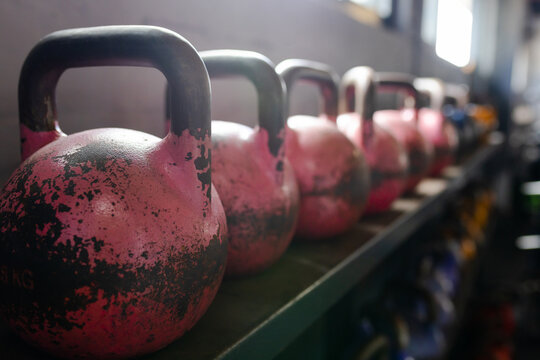 Worn pink kettlebell resting on metal rack, showing chipped paint and handle glow from window