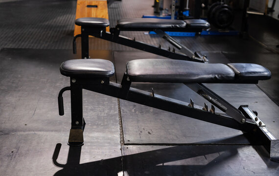 Adjustable bench sitting on rubber mats in gym free-weight area, casting long shadows with plyo box