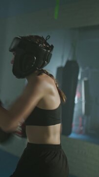 Aggressive fight, woman pro fighter wearing protective helmet, hard training in the boxing gym, train defense and series of punches on a battle, vertical video.