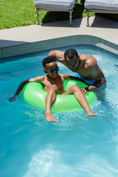 African American father and son playing in backyard pool with green ring and sunglasses
