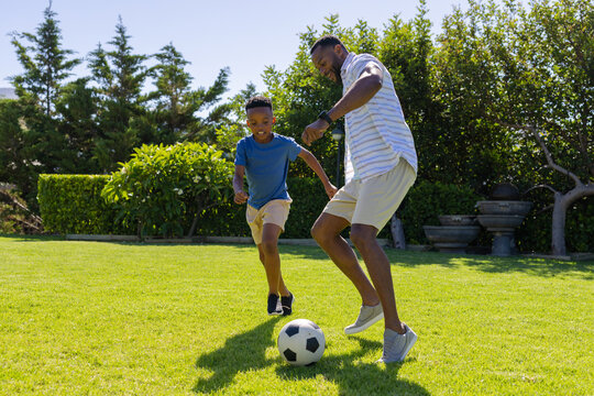 African American father and son playing soccer on backyard lawn, controlling ball with sneakers
