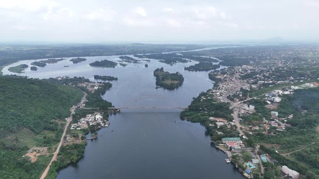 Cinematic drone shot capturing the iconic Adomi Bridge over the Volta River in Akosombo, Ghana. High-angle perspective of West African infrastructure and lush river landscape
