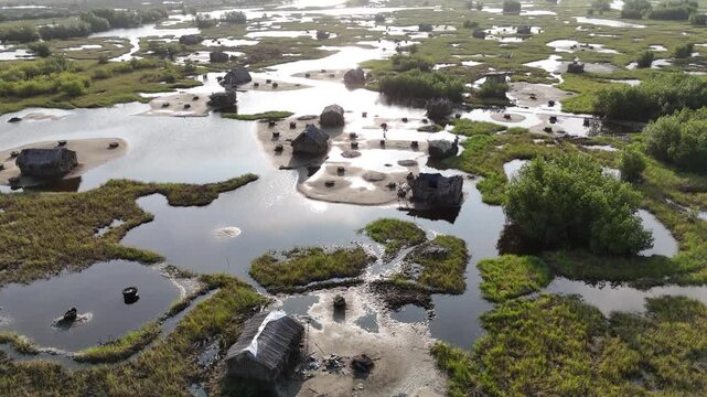 drone shot of the coastal marshlands in Ouidah, Benin. Features traditional thatched huts surrounded by winding water channels and lush green vegetation