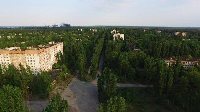 Aerial view of abandoned city reclaimed by nature, with nuclear containment structure visible in the distance.
