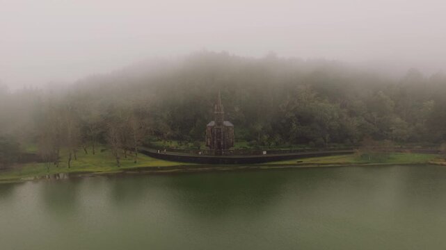 Aerial view of Capela Nossa Senhora das Vitorias beside Furnas Lake surrounded by forest and mist on foggy day Sao Miguel Island Azores Portugal