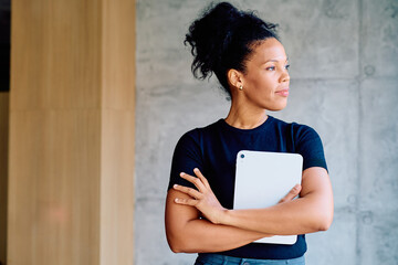 Professional businesswoman looking away planning future strategies. She is holding a tablet with arms crossed, thinking with focus © we.bond.creations