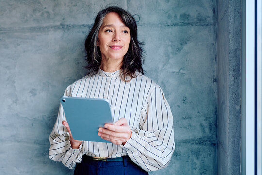 Experienced professional woman with grey hair holding a digital tablet. She is smiling, looking hopeful for the future