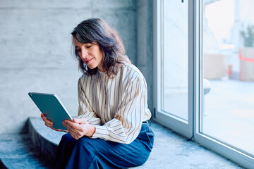 Woman sitting on steps using a digital tablet for work or communication, reflecting modern...