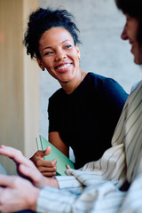 Happy black woman holding a notebook and smiling while listening to a colleague during a...