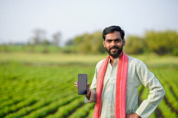 Fototapeta premium young indian farmer showing smartphone screen standing at green peanut field